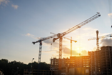 Poster - Cranes lift materials at a bustling construction site as the sun sets, signaling the end of a productive day in building development