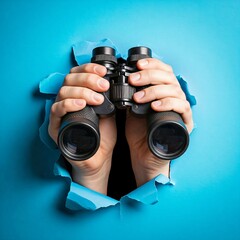 People hands holding a binocular coming through blue torn paper background 