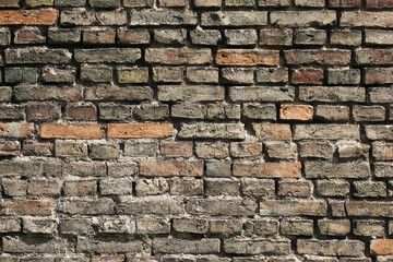 Aged brick wall of an old tenement house. Cracked and chipped surface with grunge texture. Historic building with weathered bricks. Rustic, scratched facade showing signs of decay.