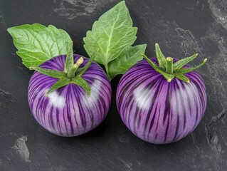 Wall Mural - Two purple-striped tomatoes with green leaves on dark grey background