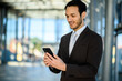 © Minerva Studio - Smiling young executive checking his phone in a modern office setting