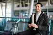 © Minerva Studio - Smiling businessman using smartphone at airport