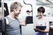 © STEEXBuyout/peopleimages.com - Personal trainer, clipboard and people with workout in gym for training equipment, coaching or notes. Man, fitness and woman with checklist in session for exercise, help or tracking progress on paper