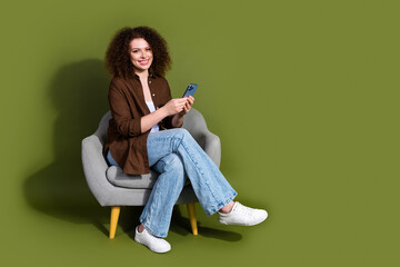 Wall Mural - Full size photo of pretty young woman sit chair smart phone empty space isolated on khaki color background