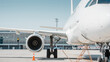 © andrbk - Front view of passenger aircraft - right side. Close-up view of white aircraft on airport apron: fuselage, landing gear, turbofan engine nacelle and wing.Airport terminal in the background.