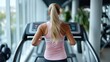 © Pinklife - The image depicts a blonde woman with a ponytail running on a treadmill in a modern, well-lit fitness gym. Her posture and the equipment are captured from behind.