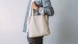 © DYNECREATIVE - Minimalistic image of a man carrying a plain beige tote bag on his shoulder, standing against a white background.
