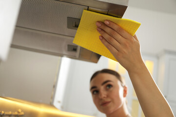 Canvas Print - Beautiful young woman cleaning kitchen hood with napkin at home, selective focus