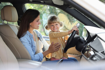 Wall Mural - Happy woman with her daughter holding steering wheel inside car