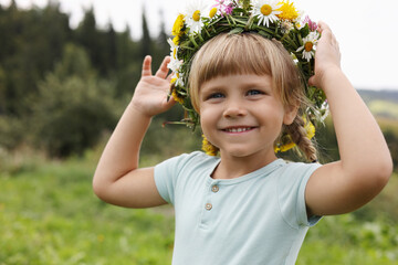 Wall Mural - Portrait of smiling little girl in floral wreath outdoors, space for text. Child enjoying beautiful nature