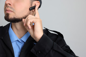 Wall Mural - Security guard in uniform with earpiece on grey background, closeup