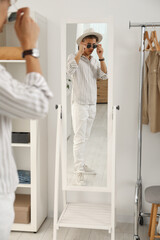 Poster - Handsome man in hat and glasses looking at mirror indoors