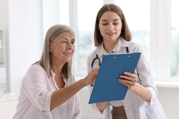 Canvas Print - Smiling healthcare worker with clipboard consulting senior patient in hospital