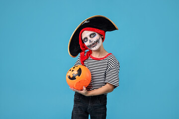 Wall Mural - Funny boy with pumpkin bucket dressed like pirate on light blue background. Halloween costume