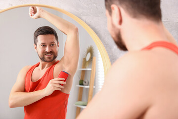 Wall Mural - Smiling man applying solid deodorant near mirror at home