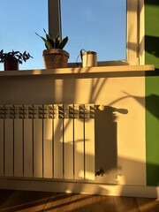 White heating radiator mounted on a white wall, illuminated by sunlight, casting beautiful shadows. This image captures the interplay of light and warmth in a cozy interior setting. Vertical photo