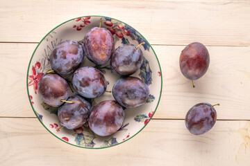 Wall Mural - Ripe plums in a ceramic dish on a wooden table, macro, top view.