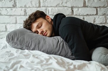 A man is sleeping on his side with a stuffed animal and a pillow. He is wearing gray pajamas with a hood, against a white background. Advertising stock photo. Close-up of both hands holding a pillow