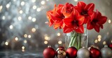 Red amaryllis flowers in a glass vase surrounded by holiday ornaments