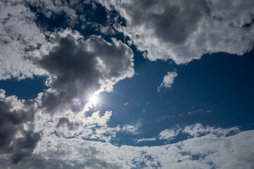 Blue sky with dark clouds and partly covered sun with sunbeams