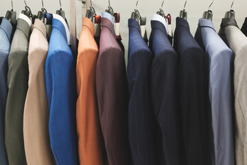 Poster - A row of suits hanging on a rack, with the blue suit on the far left and the brown suit on the far right