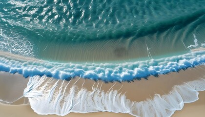 Aerial view of sandy beach with light blue waves sparkling under sunlight