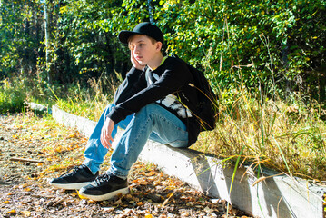 sad thoughtful boy, schoolboy, teenager sitting in park in autumn