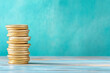 © ChaoticDesignStudio - A stack of golden coins on a wooden surface against a blue-green backdrop in soft lighting