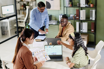 Aufkleber - Group of co-workers interacting in modern office with open laptops on table, discussing project details. Diverse team utilizing documents and charts during work meeting