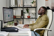 © pressmaster - Man sitting at desk using computer for data analysis in modern office environment with bookshelves and greenery in background