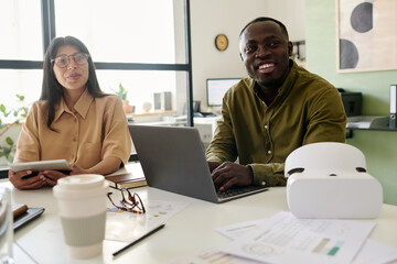 Aufkleber - Two colleagues, one Black person and one Caucasian, smiling and collaborating on project with laptop and documents on table, enjoying bright and open workspace