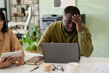 Aufkleber - African American man and Asian woman working together with laptop and tablet, inside modern office environment with several documents and electronic devices on table both focused on screens