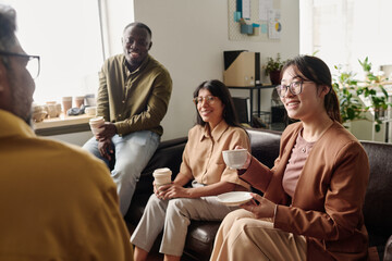 Aufkleber - Group of diverse colleagues sitting on couch, smiling and holding coffee cups in bright office setting, creating positive and relaxed atmosphere