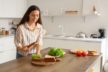 Wall Mural - Young woman making tasty sandwich in kitchen