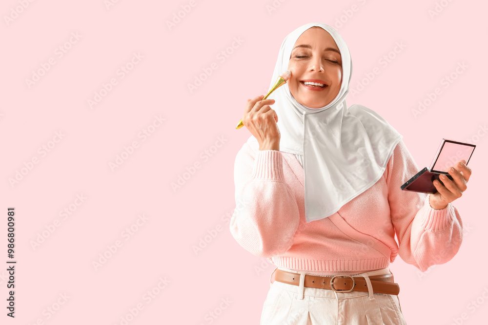 Mature Muslim woman doing makeup on pink background