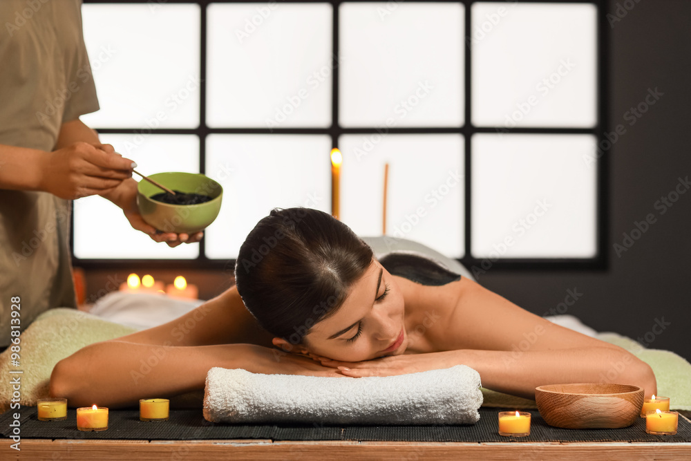 Young woman undergoing mud treatment in dark spa salon