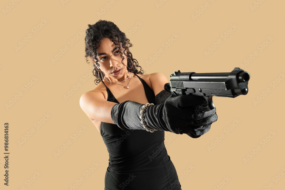 Beautiful African-American spy with gun on beige background