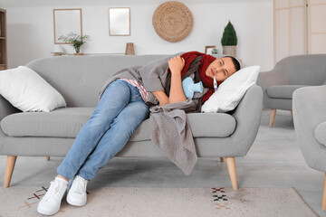 Wall Mural - Ill young man with hot water bottle and thermometer measuring temperature on sofa at home