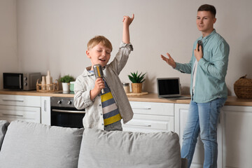 Poster - Noisy little boy singing with microphone and his father working in kitchen