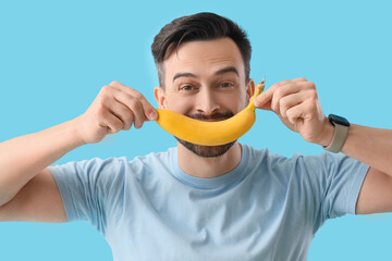 Canvas Print - Young man with banana on blue background, closeup