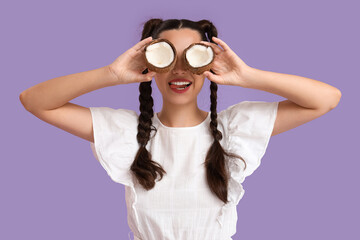 Poster - Beautiful young happy woman with braids holding halves of fresh coconut on purple background