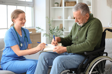 Wall Mural - Senior man suffering from Parkinson syndrome in wheelchair with nurse drawing on notebook at home