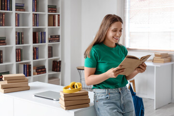 Poster - Happy female student with headphones reading book while studying at library