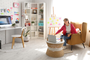 Canvas Print - Female graphic designer working with tablet in armchair at office