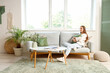 © Pixel-Shot - Young woman with soft pillow sitting on grey sofa in living room