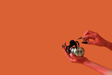 Devil hands with spider and pumpkin on orange background. Halloween celebration