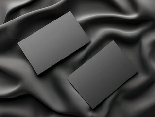 Two blank black business cards on a smooth black silk fabric background.