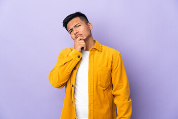 Young Ecuadorian man isolated on purple background having doubts