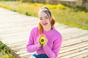 Poster - Young pretty girl at outdoors holding an avocado with happy expression