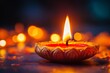 © Darya Lavinskaya - A close up of a single diya glowing warmly with a bright flame, surrounded by soft bokeh lights